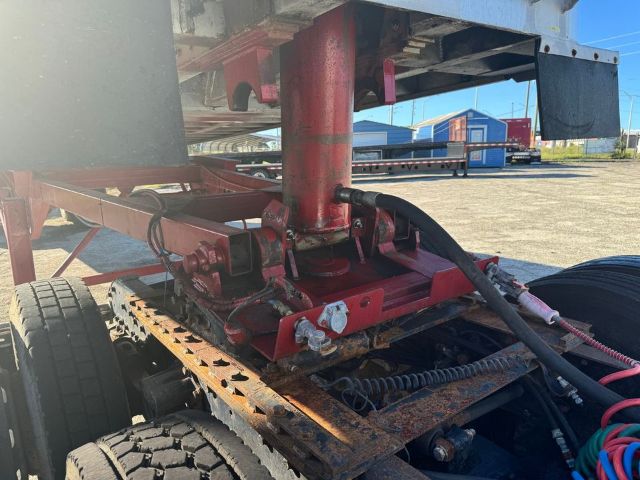 GMC trailer chassis with red painted hydraulic legs and frame; various hoses and mechanical components visible near the rear axle; rust on metal components.