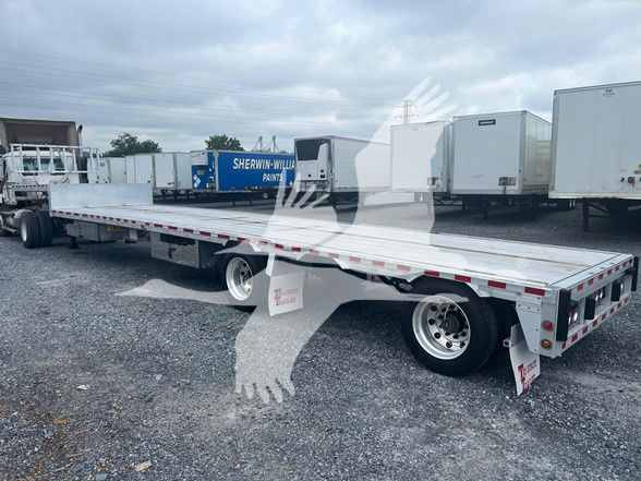 2019 Reitnouer Dropmiser flatbed trailer showing long flat deck, drop deck, dual rear axles with chrome wheels, reflective tape, and mud flaps.