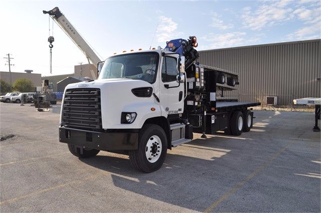 Truck cab with knuckle boom crane mounted at rear, white cab, black chassis, crane arm raised in background.