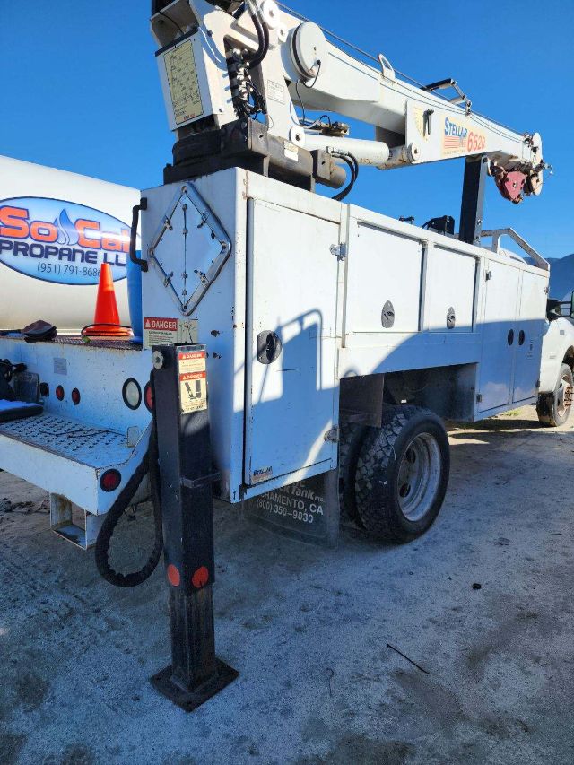 Ford F-550 utility bucket truck with mounted crane, white workbody, stabilizing leg extended, rear wheels, ladders, and warning decals visible.
