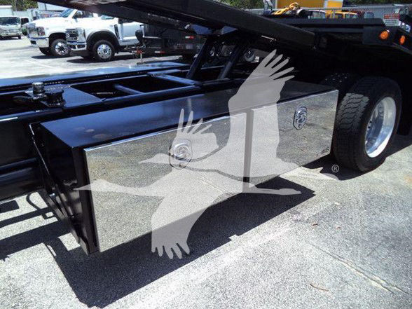 Truck bed with a large metal tool/storage box mounted under flatbed, bumper-wheel area visible on right, glossy chrome finish with reflection.