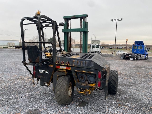 Kesmac F5000 forklift showing rear view with roll cage and tires, faded black and yellow body, and hydraulic mast in green in background.