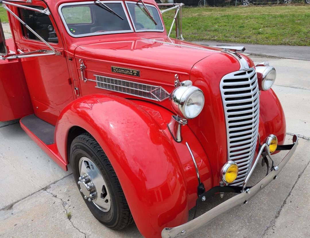 Diamond T hauler truck front-left view showing chrome grille, round headlights, red body, white grille bars, Diamond T badge on side, yellow fog lamps, and chrome bumper.