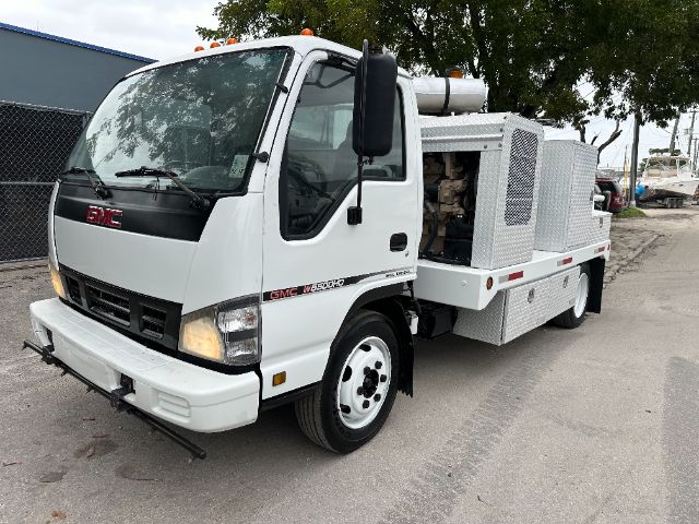 GMC W5500 tow/utility truck side view showing white cab and aluminum service body with diamond plate compartments.