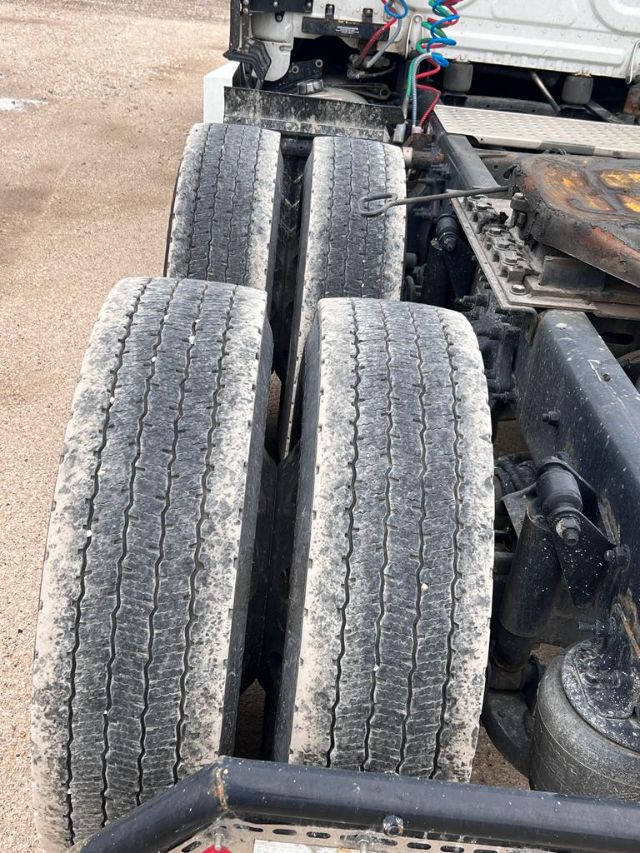 Tractor-trailer rear axles with dual tires and visible suspension components. Worn tread on tires, wiring harness, and chassis nearby.