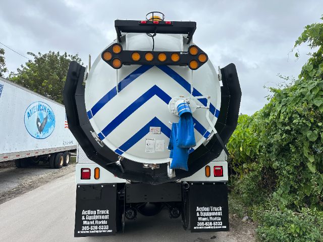 Back view of a Freightliner vacuum truck with chevron reflective stripes on a cylindrical tank, blue cover over a connection, two black mud flaps with white text, and multiple lights.