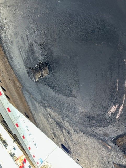 Trailer underside with painted dark surface and a small rectangular opening; partial wheel or frame visible; curved surface with textural wear.
