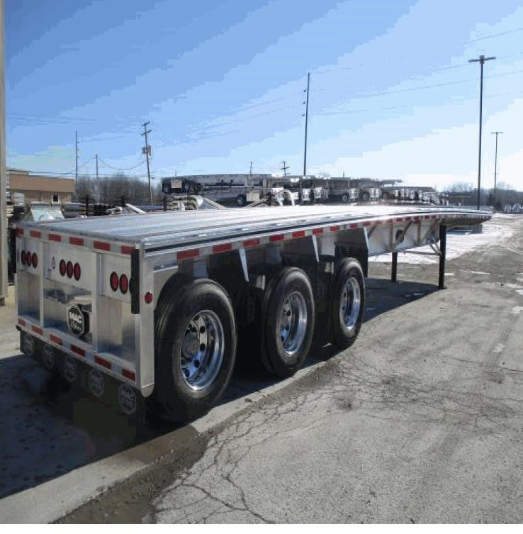Tri-axle flatbed trailer with three axles and polished aluminum sides, rear with multiple red tail lights, reflective safety tape along sides.