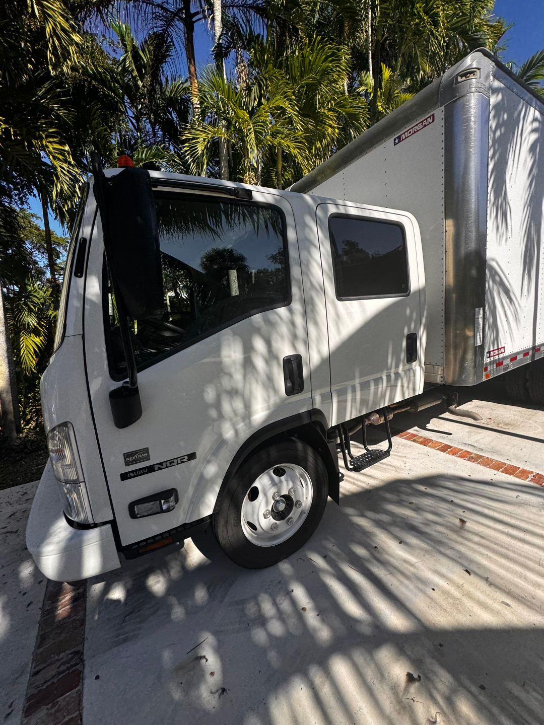 Isuzu NQR box truck side view with cab and Morgan dry van trailer, front wheel visible, logo badges on door.