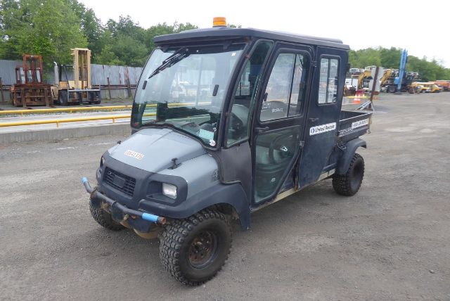 Club Car Carryall 1700 utility vehicle in a yard, front left view showing cab, doors, bumper, and tires.