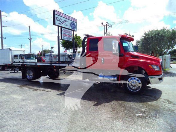 2024 International MV tow truck in red with a long flatbed, side view shows cab and front grille.