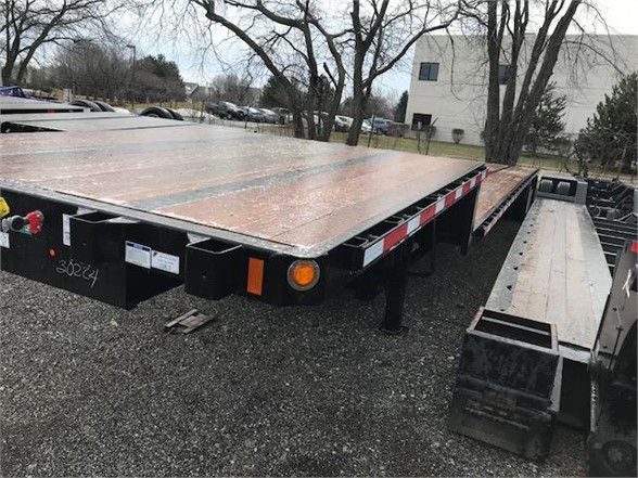 Flatbed trailer with wooden deck and rear taillights, low-angle view showing end platform and hitch area, Fontaine VELOCITY trailer in background.