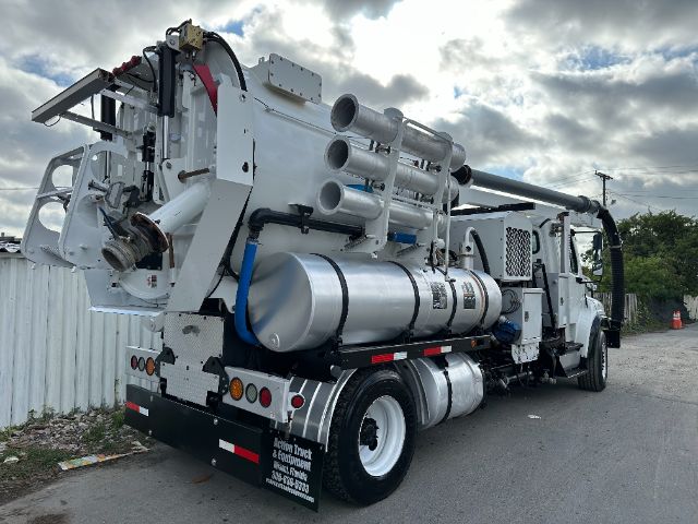 Freightliner M2 vacuum truck with large cylindrical tanks and piping mounted on the bed, side view showing rear wheels and equipment racks.