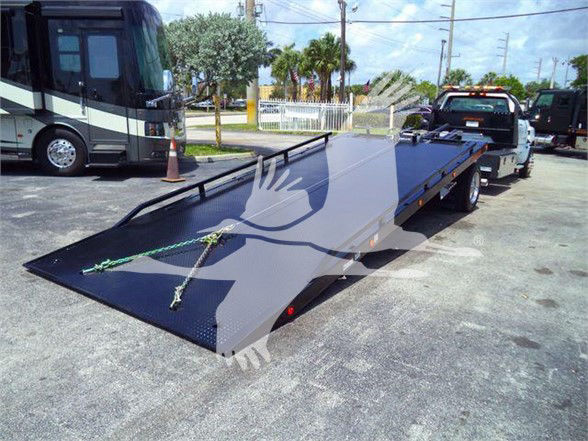 Truck tow bed with a long black flatbed trailer, some rigging straps, and a vehicle in the background.
