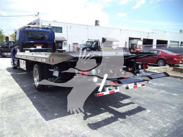 Tow truck flatbed rear view with blue winch cab; MV607EXCABBLU stock tag. No visible fluid labels or part numbers.