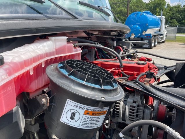 Freightliner M2 engine bay showing air inlet manifold heater housing with label and red engine components.
