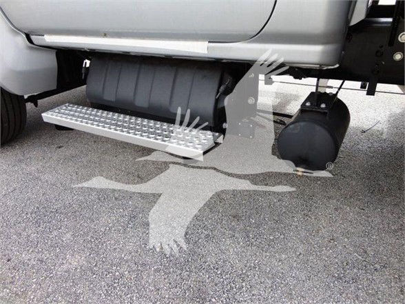 A side view of a 2023 Chevrolet Silverado 6500HD flatbed truck showing a metal running board/steps under the cab and a large black fuel tank.