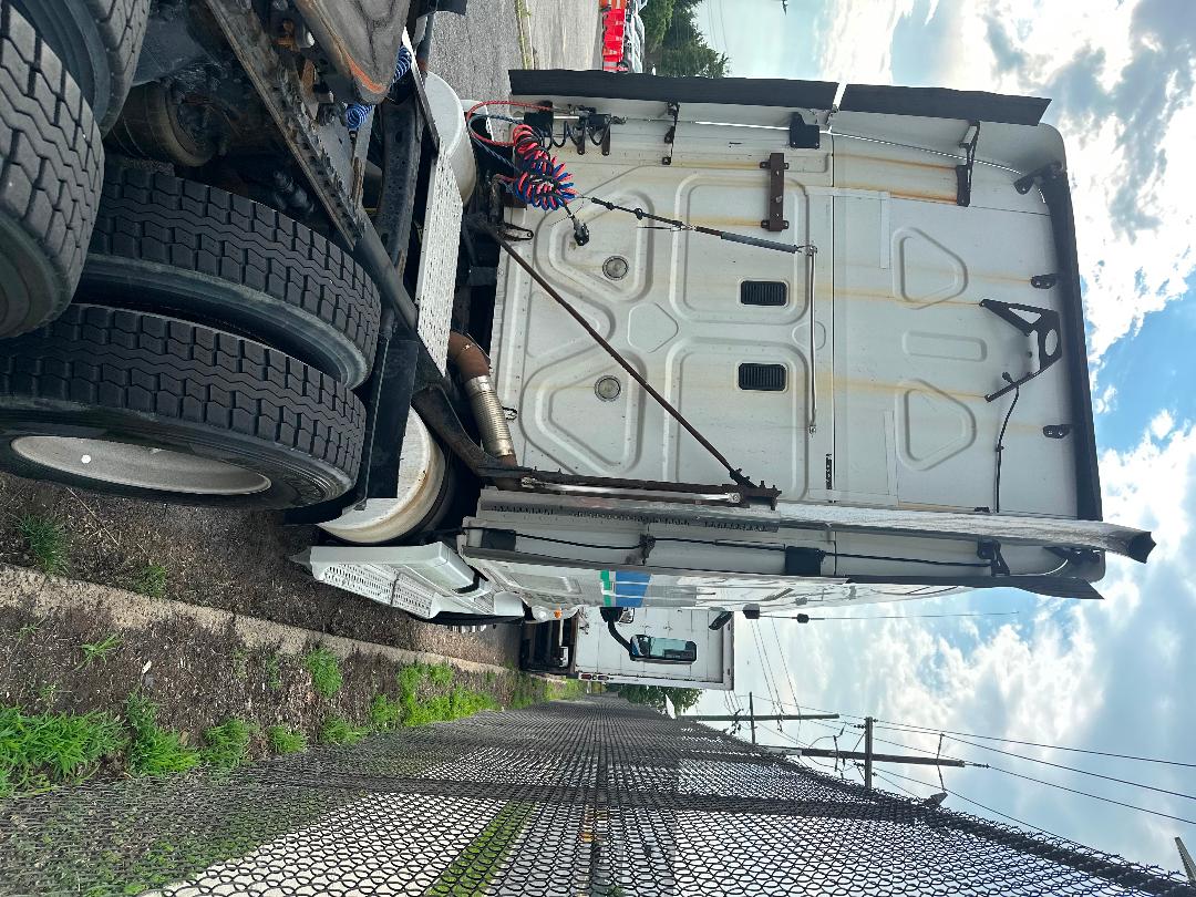 Freightliner Cascadia truck rear cab area with dual rear wheels, exhaust pipe, and rear doors visible; white sleeper tractor in a lot.
