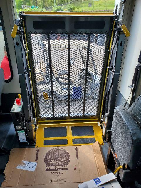 Ford E-450 shuttle bus interior showing wheelchair lift/station with safety gate and yellow floor markings.