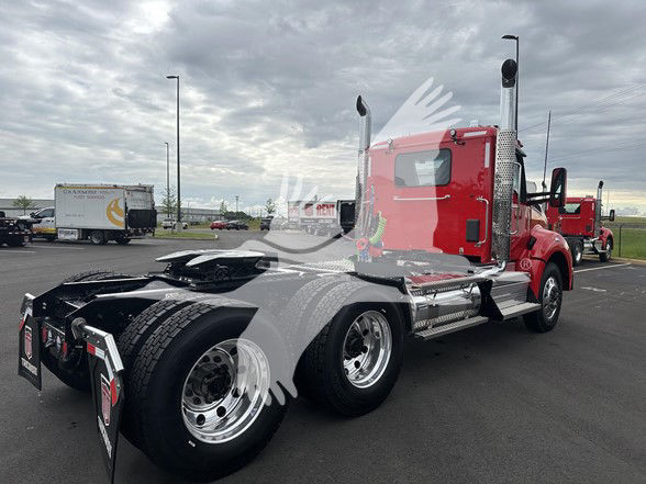 Kenworth T880 conventional daycab tractor showing red cab and dual rear axles with chrome exhaust stacks.