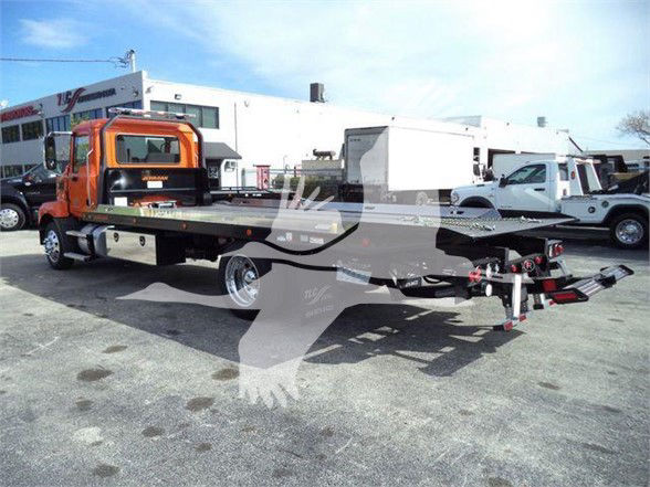 Mack MD6 tow truck with flatbed, orange cab, long flatbed and equipment compartments visible.