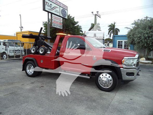 Red Ram 4500 Tow Truck with a wheel lift in the bed; showroom lot in background. Visible text includes a signboard reading TLC and other dealership signage; no other legible labels on vehicle surfaces.