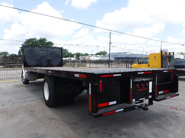 Flatbed truck trailer with International 4300 cab in background, black flatbed with red-and-white reflective tape, loading area and rear tools.