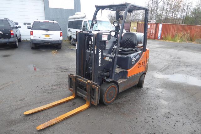 Doosan GC25P-5 forklift side view showing orange/black body and long forks in a yard.