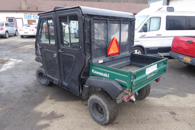 Kawasaki KAF950G utility vehicle with enclosed cab and green cargo bed, rear view showing spare wheel, triangle reflector, and black mesh cab rear.