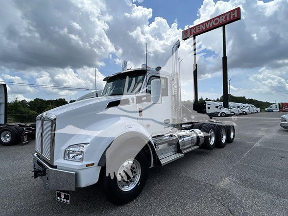 Kenworth T880 conventional daycab truck in dealership lot, white, with Kenworth sign in background.