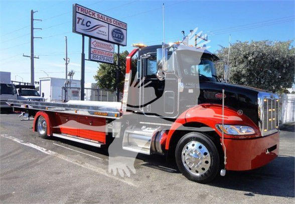 Peterbilt 337 tow truck with chrome wheels and red and black cab. Side shows flatbed. Signage in background reading Truck Sales Center, TLC, Jerry’s, 954-977-?? (partial).