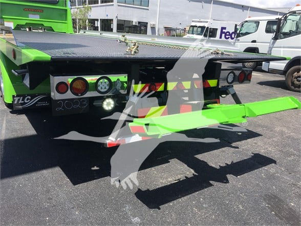 Tow truck bed of a green 2022 Peterbilt 337 with rear loading platform and bumper, visible lights, and reflective safety markings.