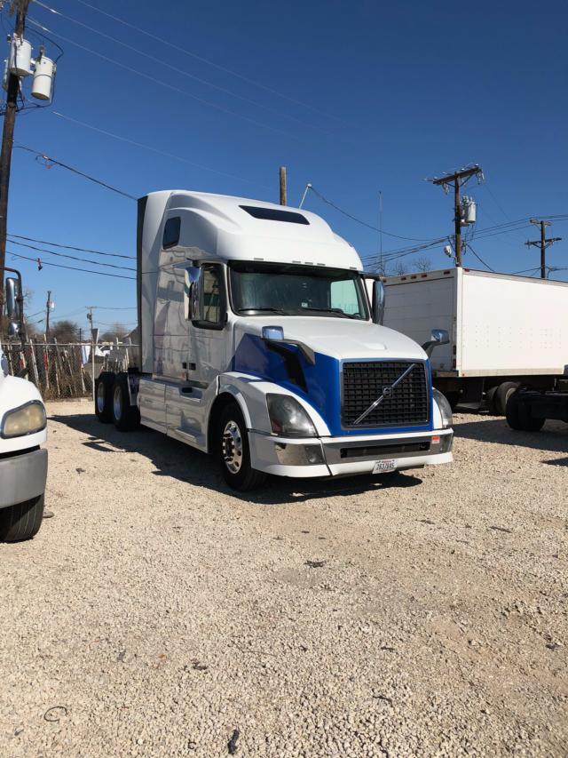 2013 Volvo VNL64 conventional sleeper truck in a gravel lot, white with blue accents, front grille and cab details visible.