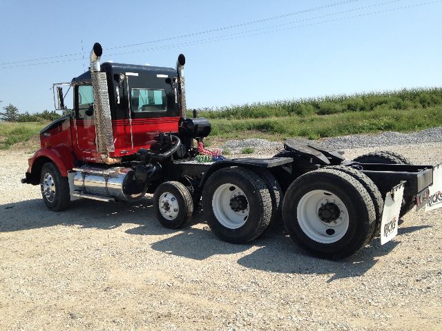 Kenworth T800 tractor cab showing side exhaust stacks, red cab, and dual rear axles with white wheels.