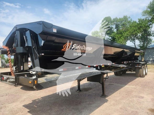 SideDump dump trailer showing black hopper with SideDump logo and contact number, twin axle with landing gear, in outdoor lot.
