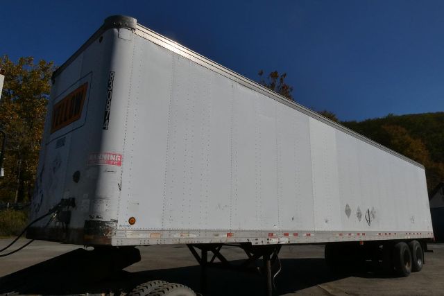 Trailer side view showing white Fruehauf trailer with orange sign and multiple wheels.
