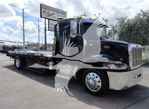 2022 Peterbilt 337 tow truck in a dealership lot with long flatbed and chrome wheels.