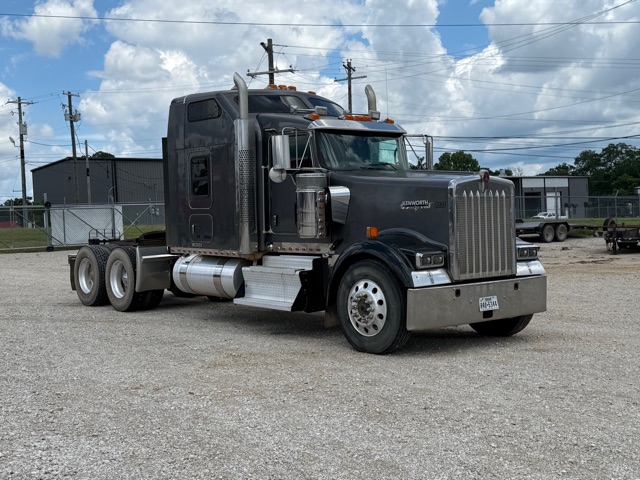Kenworth w900 conventional sleeper truck in a gravel lot with chrome exhaust stacks and grille, dual rear axles, and fuel tanks visible