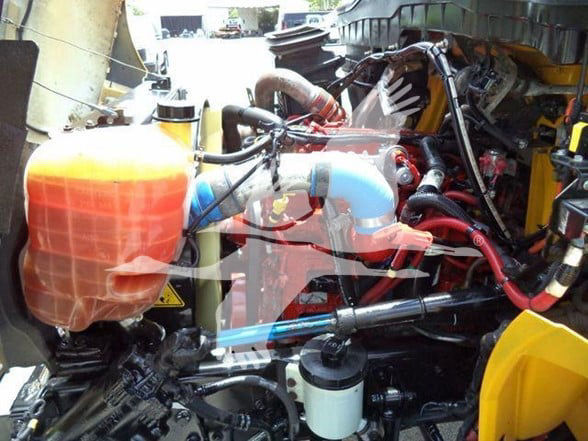 Truck engine bay showing coolant reservoir and various hoses and hydraulic lines.