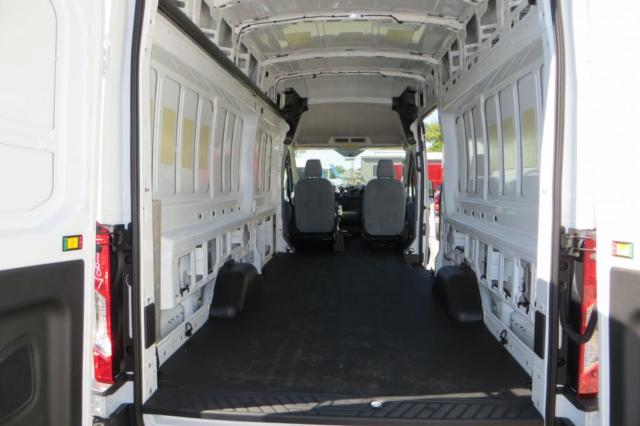 Ford Transit van interior cargo area with two front seats visible, empty cargo space, white panel walls, overhead roofing, rear doors open.