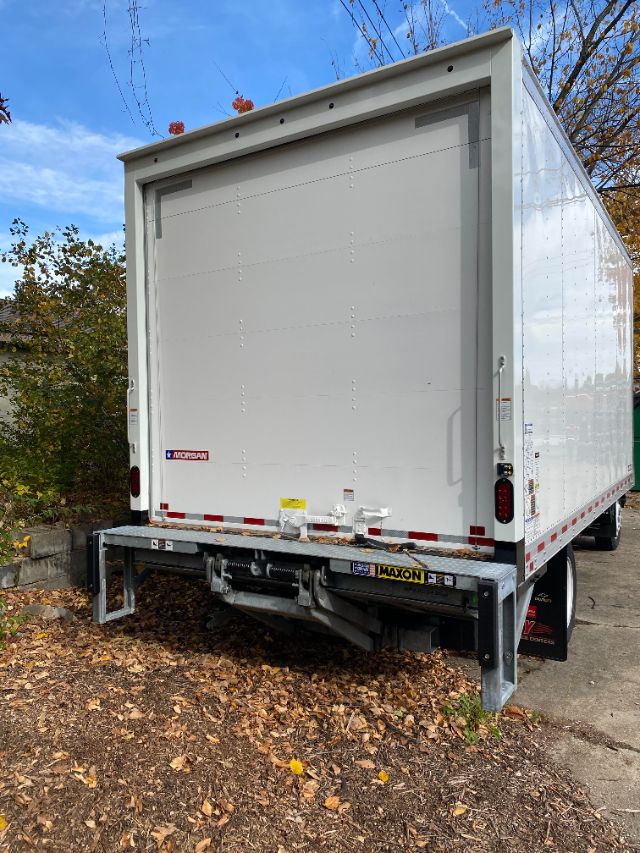 Isuzu NRR cab chassis box truck rear view showing closed roll-up cargo door, Maxon rear stabilizer bar, and bumper with reflectors.