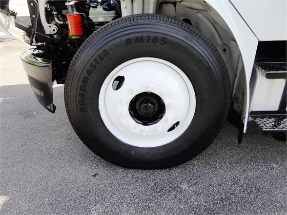 Truck front wheel showing tire with text 'ROADMASTER RM185' on the sidewall and white steel wheel with lug nuts; partial truck components visible at wheel well.