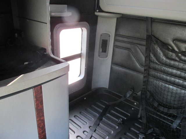 Truck cab interior showing sleeper area with door window and side panel, horizontal metal floor, and a black quilted seat cover or padding.