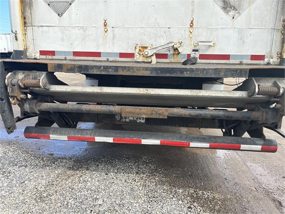 Rear view of a Wabash dry van trailer showing the liftgate/roll tarp mechanism and undercarriage with rust and support beams.