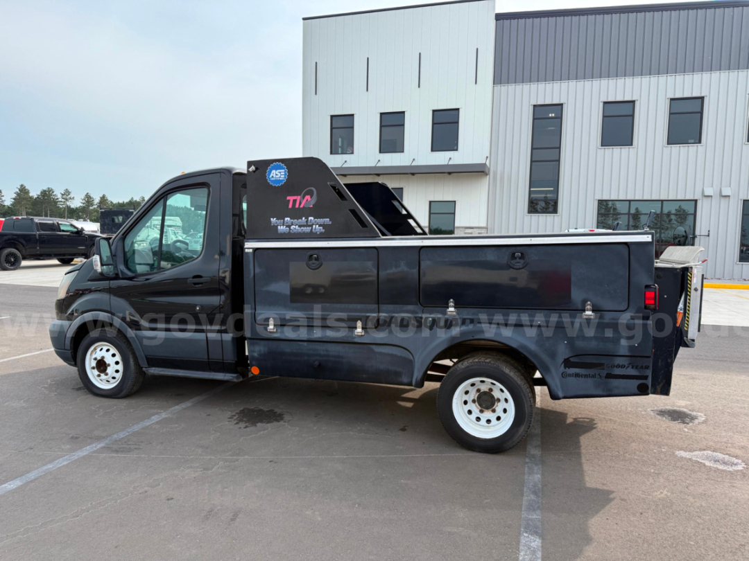 Ford Transit utility truck with black service body, side drawers, and elevated crane rack. Side text includes ASE badge and equipment branding.