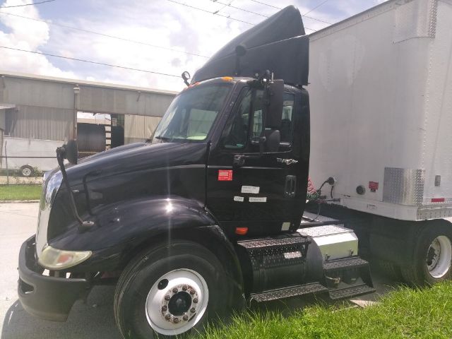 Black International truck tractor cab in front of a white trailer, side steps, hood, mirrors, and aerodynamic daytime running lights visible.
