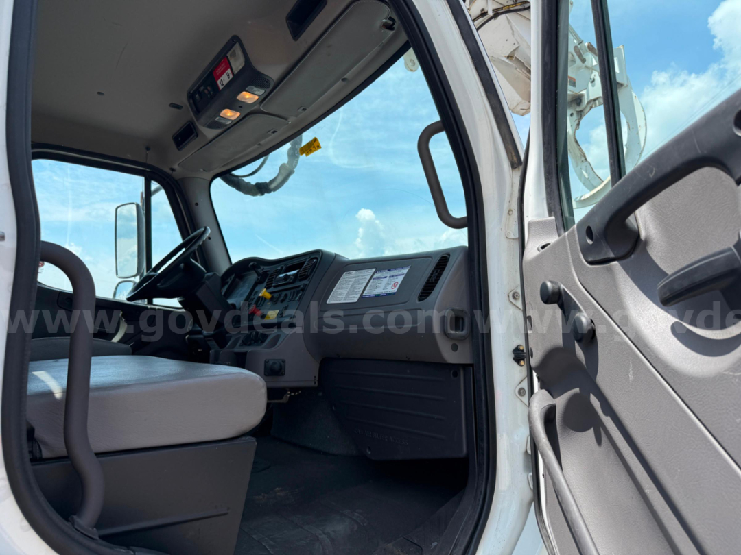 Cab interior of a Freightliner DT65 truck with steering wheel, dashboard controls, and entry door; visible window and overhead console.