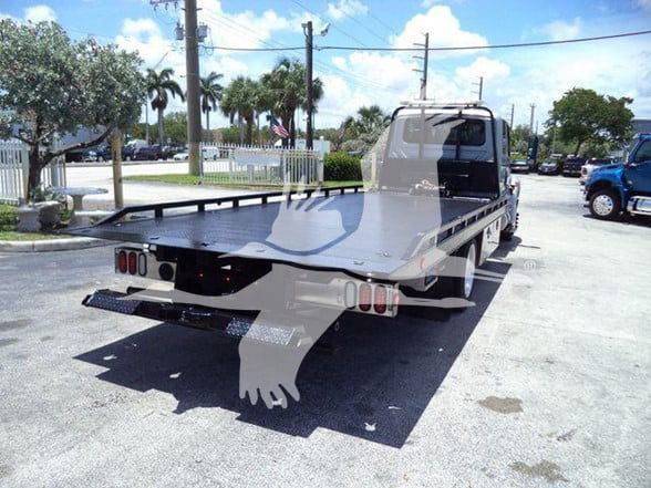 Flatbed tow truck from rear-left side showing flatbed and taillights.