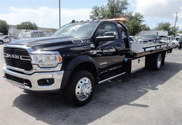 2024 Ram 5500 tow truck in black with chrome front, extended flatbed, RAM grille, dual rear wheels, orange beacon light on cab, side mirrors, running boards.