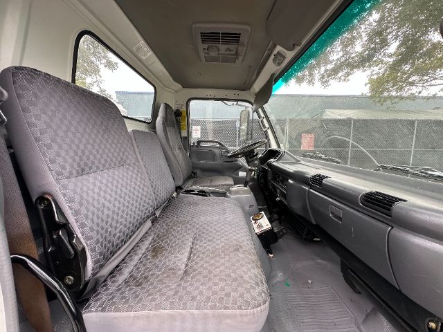 Cab interior of a GMC W5500 truck with a bench front seat and gray patterned upholstery, dashboard, steering wheel, and center console visible.